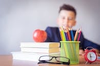 Schoolboy smiling behind a desk with books, pencils, and an alarm clock symbolizing study and creativity.